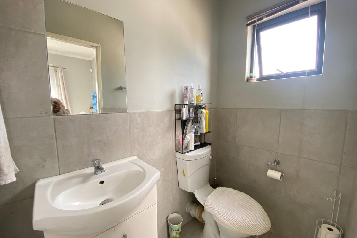 A functional bathroom featuring a vanity cabinet with a basin, a toilet, and neutral wall tiling with a top-hung window for natural light.