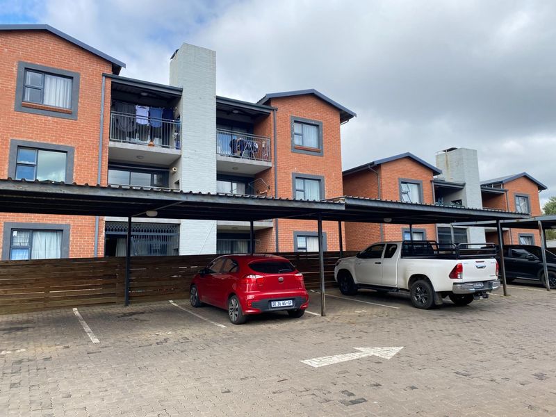 Front view of a multi-story brick townhouse complex featuring covered parking bays and private balconies.