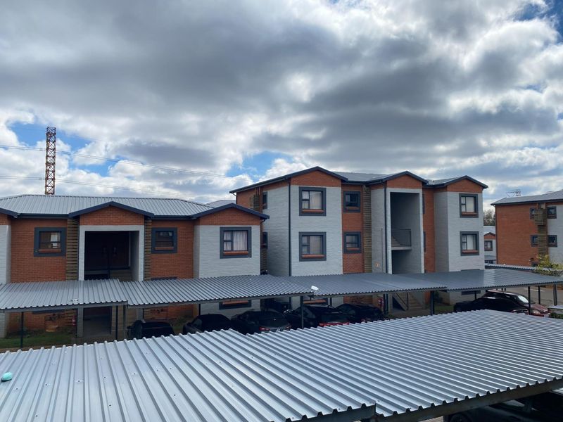 Exterior view of a multi-story townhouse complex featuring brick and painted masonry facades with covered carport parking.