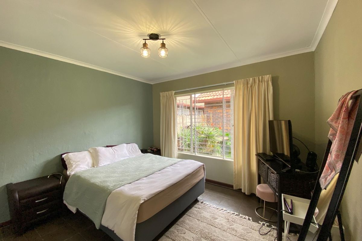 A bedroom featuring tiled flooring, a large window with security bars, and a ceiling-mounted light fixture.