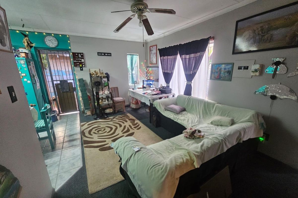 A living room area featuring a ceiling fan, tiled entryway, and access to an exterior security gate.