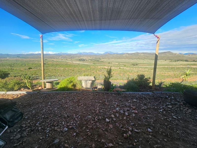 An outdoor patio area featuring a shade sail supported by timber posts, offering expansive views of the surrounding farm landscape.