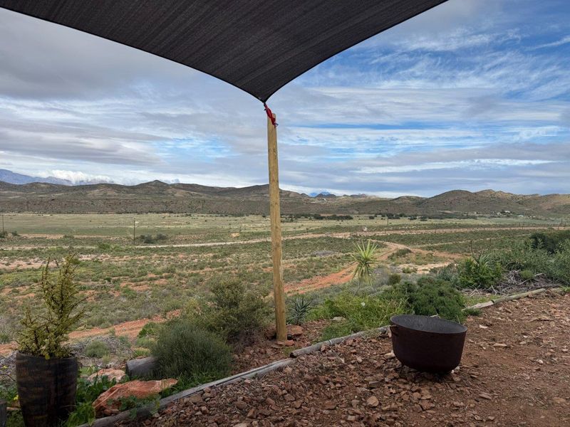 An outdoor patio area featuring a shade sail structure, offering expansive views of the surrounding rural landscape and mountain range.