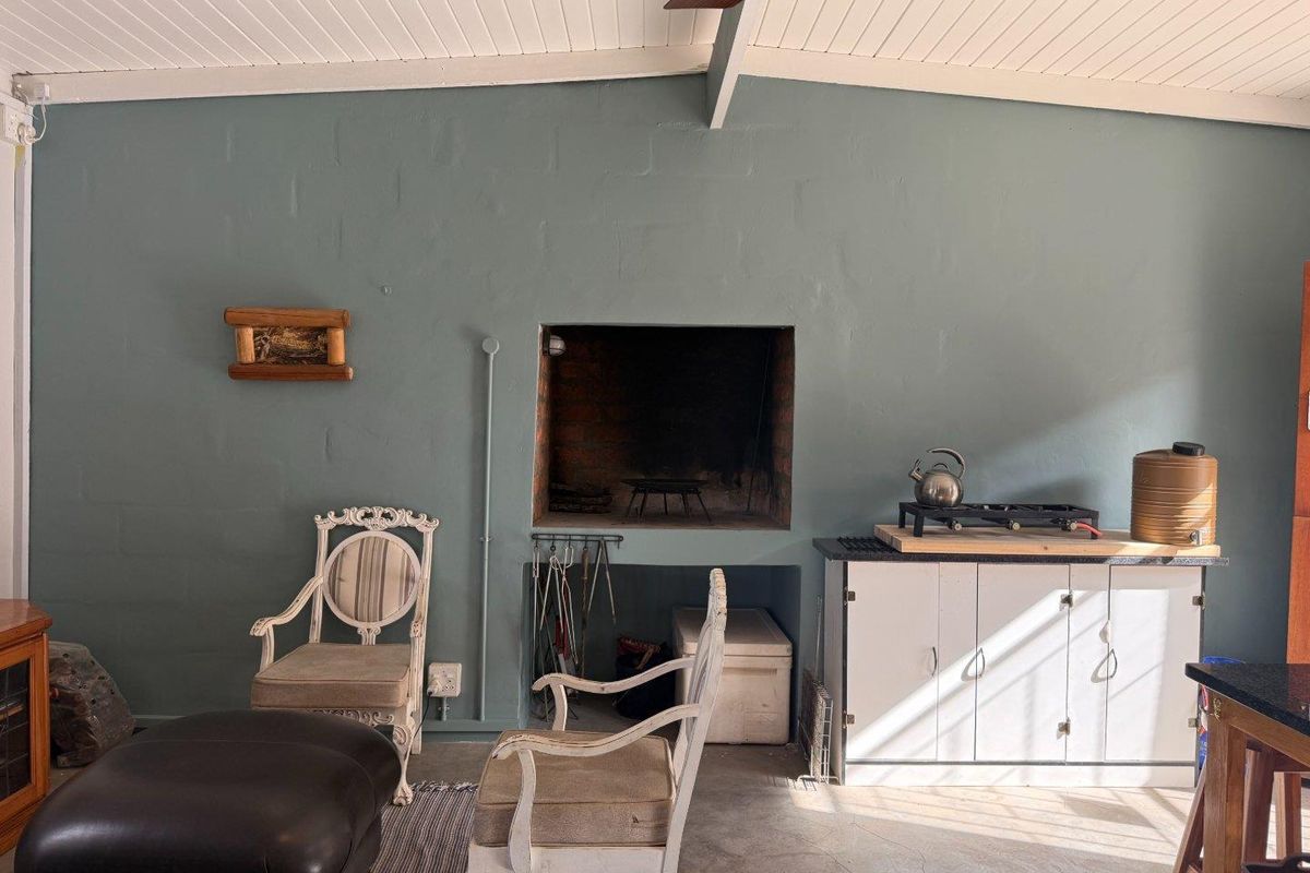A rustic indoor entertainment area featuring a built-in brick fireplace, exposed beam ceiling, and concrete flooring, ideal for cozy gatherings.