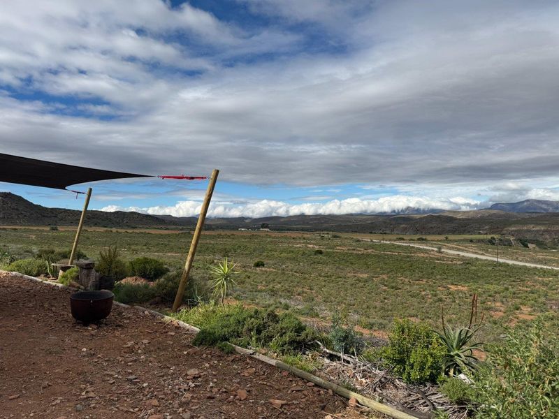 Expansive rural landscape view from a rustic outdoor patio area featuring a shade sail structure.