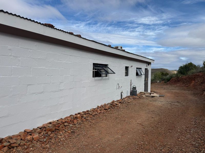 Exterior view of a white painted masonry farm building featuring corrugated metal roofing and top-hung windows, set against a rural landscape.