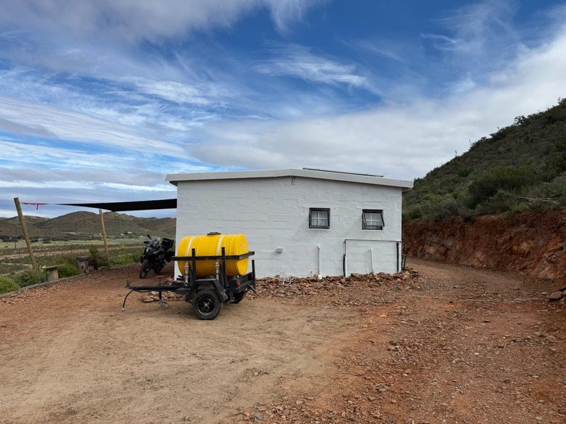 A view of a small, white-painted masonry outbuilding on a rural farm property, featuring small windows and a flat roof structure.