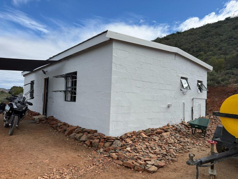 Exterior view of a simple, white-painted block structure on a farm, featuring metal roofing and casement windows.