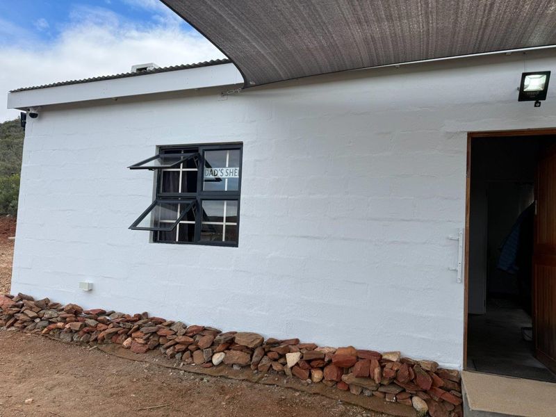 Exterior view of a farm building featuring a white painted masonry wall, dark-framed window, and a protective shade sail over the entrance.
