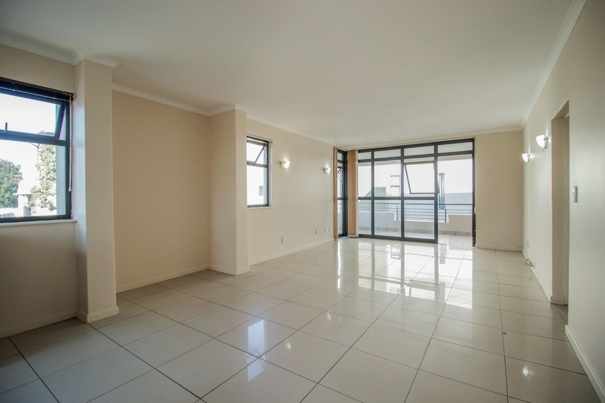 Spacious, light-filled living area featuring neutral tiled flooring, modern aluminium window frames, and direct access to an outdoor balcony through sliding glass doors.