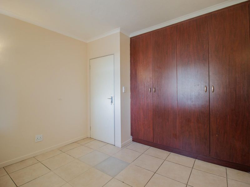 A clean, empty bedroom featuring tiled flooring and large, dark wood-finish built-in cupboards.