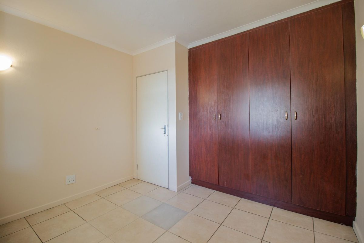 A clean, empty bedroom featuring tiled flooring and large, dark wood-finish built-in cupboards.