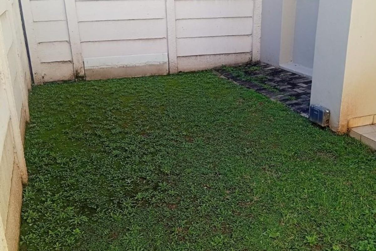 A small private rear garden area featuring a lawn, paved walkway, and enclosed by a precast concrete boundary wall.