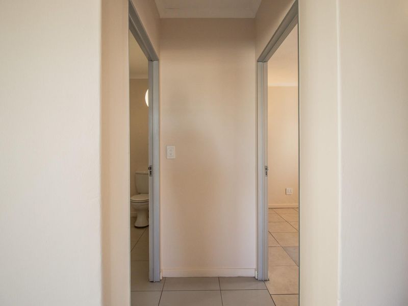 A neutral hallway featuring tiled flooring and access to adjacent rooms, including a bathroom with visible toilet fixture.