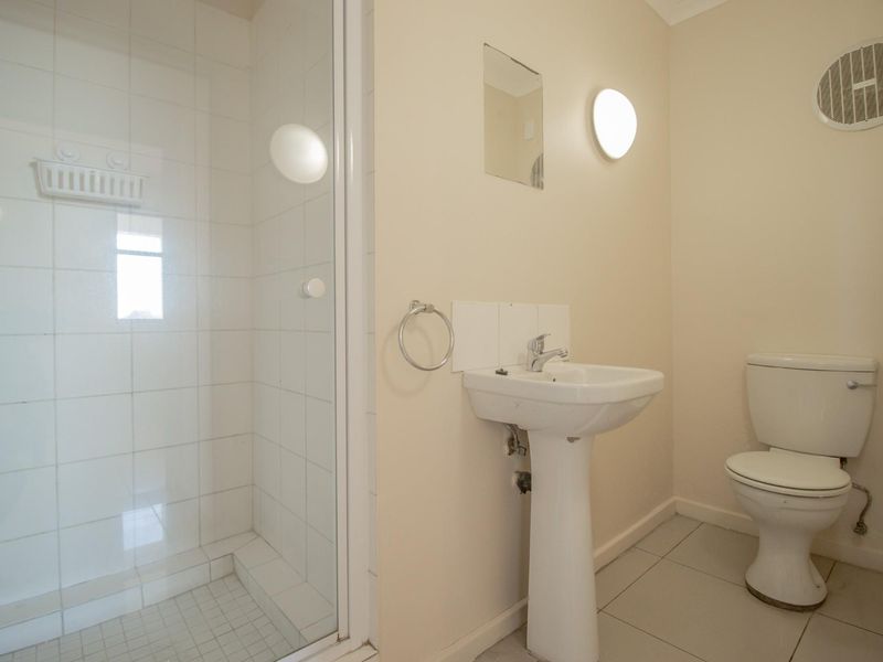A functional bathroom featuring a shower enclosure, pedestal basin, and toilet, finished with neutral wall tones and tiled flooring.