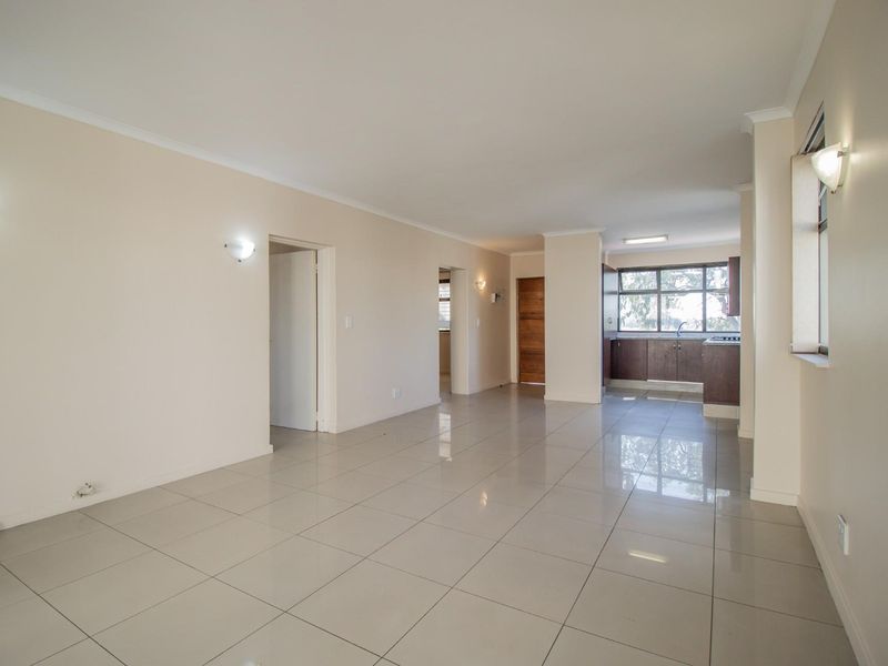 Spacious open-plan living area featuring neutral tiled flooring, wall sconces, and a functional kitchen space with built-in cabinetry.
