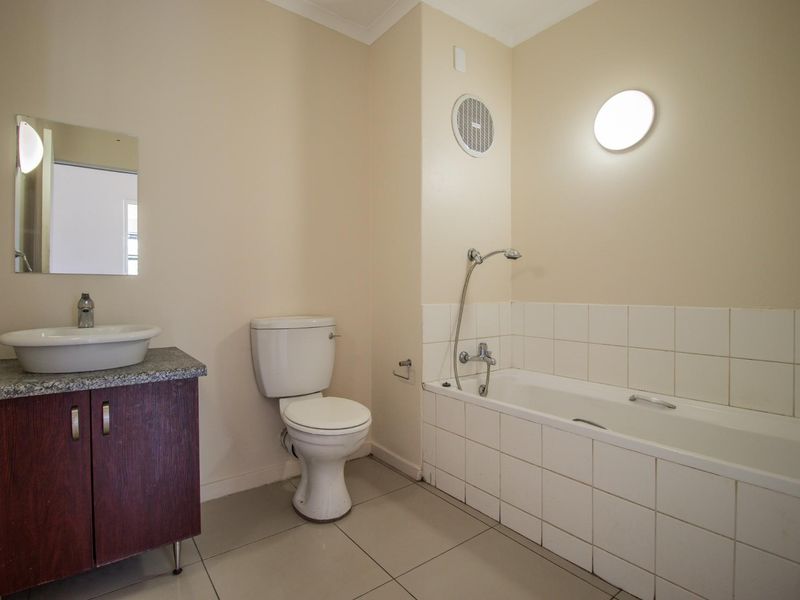 A functional bathroom featuring a vessel sink on a vanity cabinet, a standard toilet, and a bathtub with tiled surround and shower mixer.