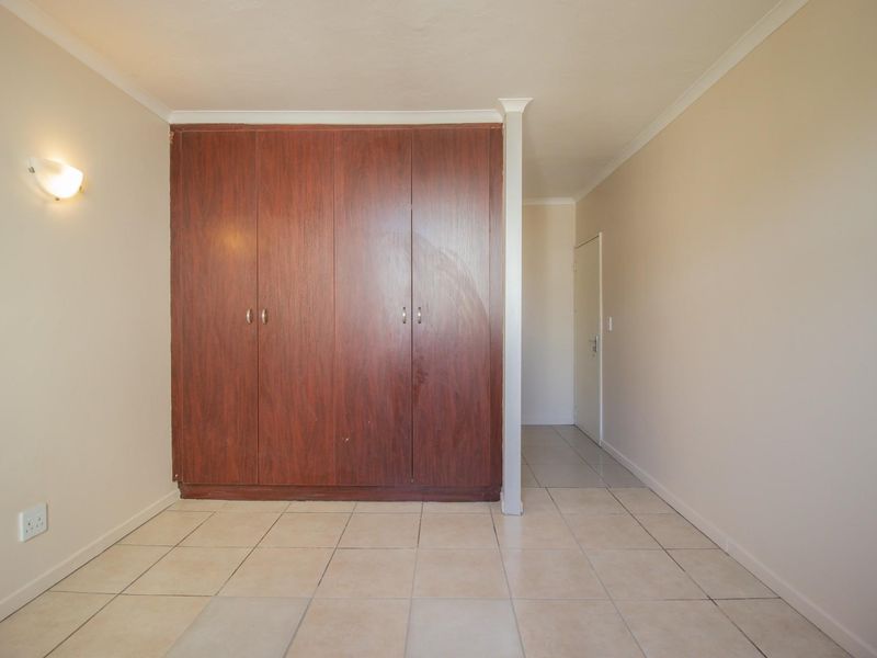 An empty bedroom featuring tiled flooring and built-in wooden cupboards, providing a neutral space ready for personalization.