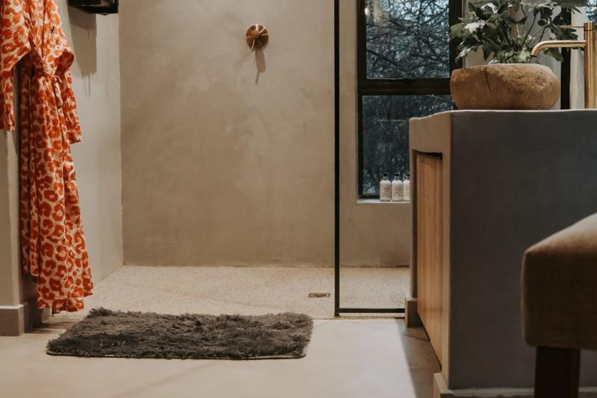 Modern bathroom featuring a walk-in shower with a black frame, brass rainfall showerhead, and a custom concrete vanity with integrated basin.