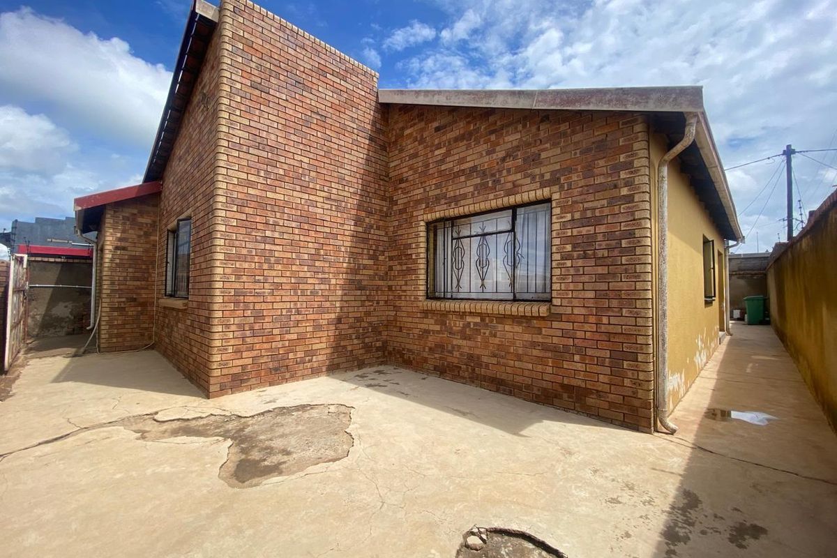 Rear exterior view of the house featuring face-brick facade, security bars on windows, and concrete paved yard area.