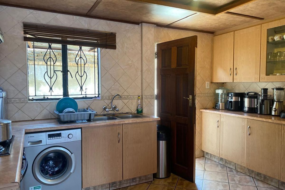 A functional kitchen featuring light wood cabinetry, tiled splashbacks, integrated laundry space, and a window with security bars.