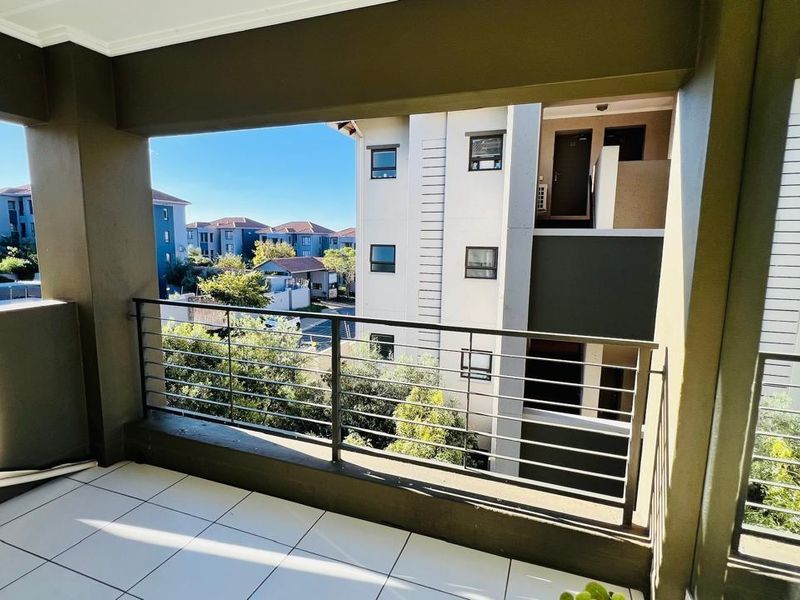 A covered balcony featuring tiled flooring and a metal railing, offering views of the surrounding apartment complex and neighborhood.
