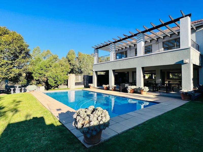 A spacious rear exterior view featuring a swimming pool, a covered patio area with a pergola, and a well-maintained garden.