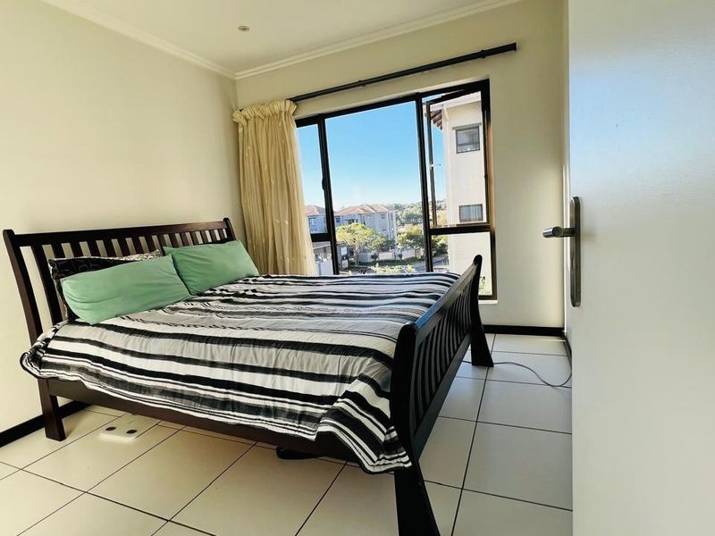 A bright bedroom featuring large windows with natural light, tiled flooring, and a neutral color palette, offering a comfortable living space.