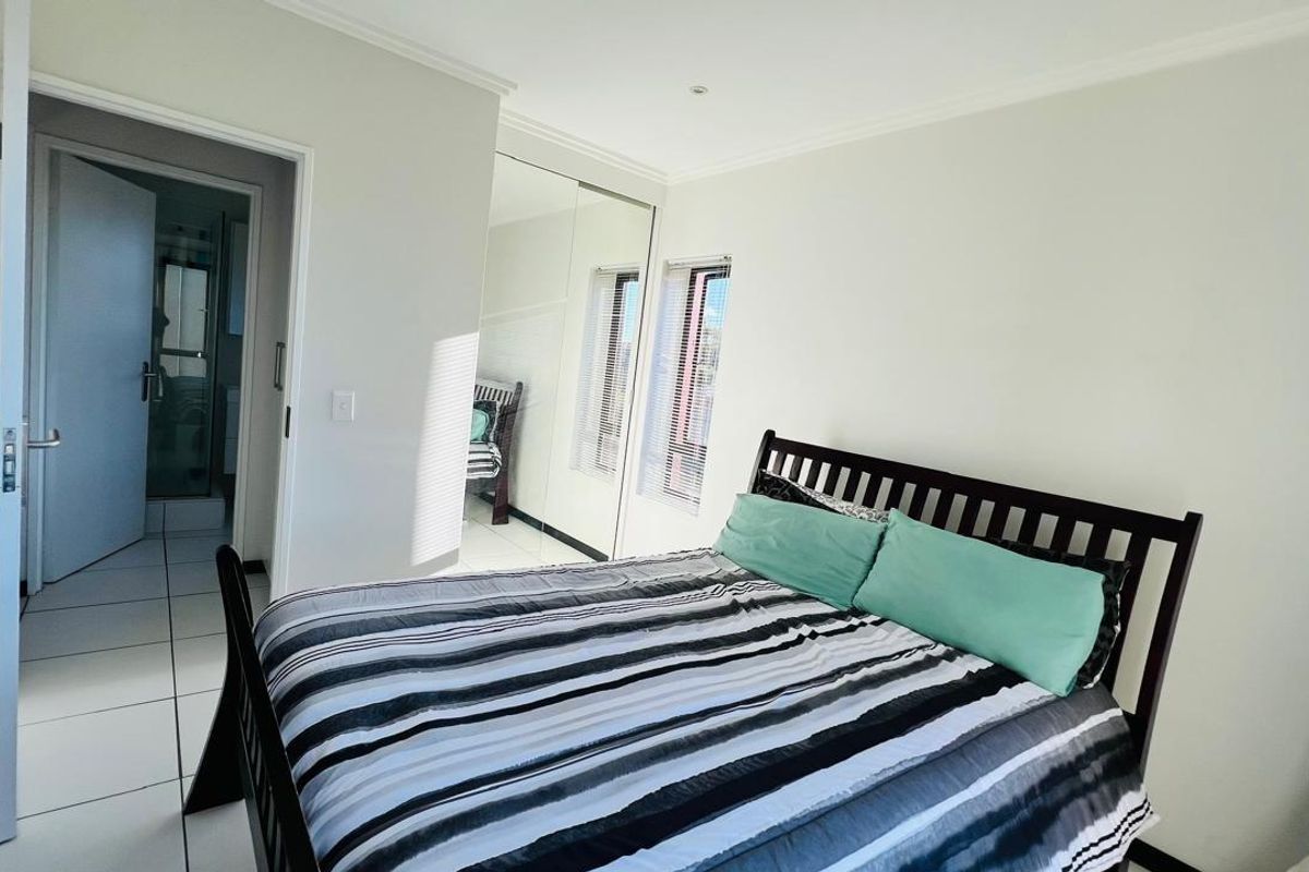 A bright bedroom featuring tiled flooring, built-in mirrored wardrobes, and an en-suite bathroom access.