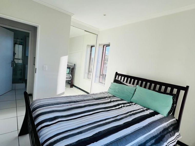 A bright bedroom featuring tiled flooring, built-in mirrored wardrobes, and an en-suite bathroom access.