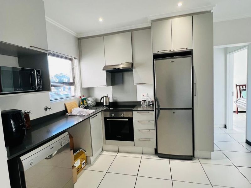 Modern kitchen featuring sleek cabinetry, dark stone countertops, built-in oven, extractor fan, and tiled flooring.