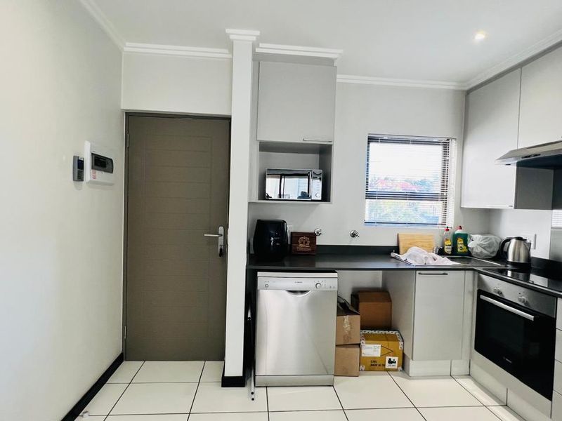Modern kitchen featuring sleek grey cabinetry, dark countertops, integrated oven, extractor fan, and tiled flooring with a convenient adjacent doorway.
