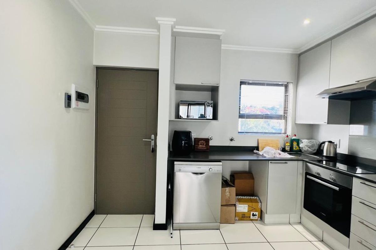 Modern kitchen featuring sleek grey cabinetry, dark countertops, integrated oven, extractor fan, and tiled flooring with a convenient adjacent doorway.
