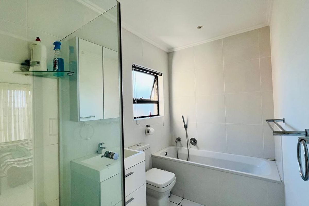 A clean, modern bathroom featuring a glass-enclosed shower, a built-in bathtub, a vanity with storage, and neutral wall tiling.