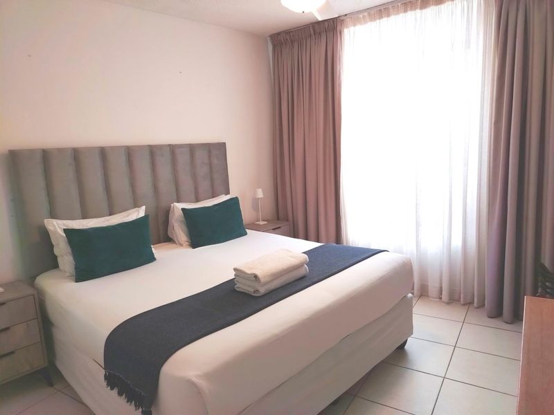 A well-lit bedroom featuring tiled flooring and floor-to-ceiling curtains, providing a neutral and comfortable living space.