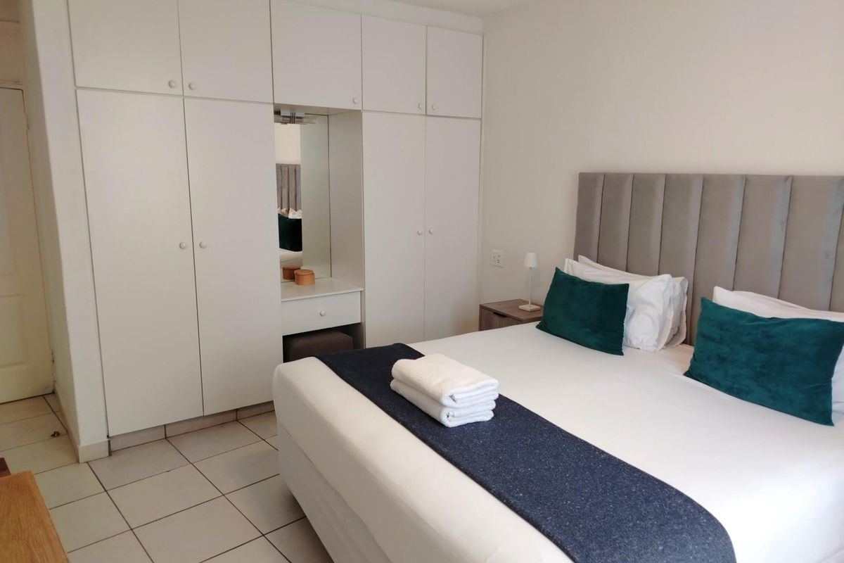 A well-maintained bedroom featuring built-in floor-to-ceiling wardrobes with an integrated vanity mirror and tiled flooring.