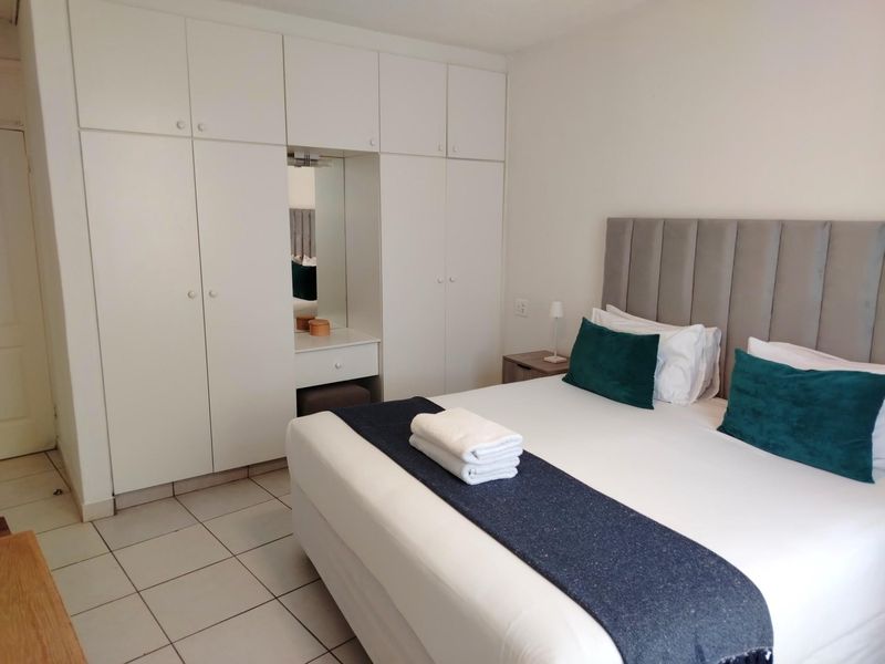 A well-maintained bedroom featuring built-in floor-to-ceiling wardrobes with an integrated vanity mirror and tiled flooring.