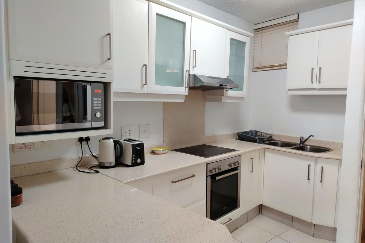 A functional kitchen featuring white cabinetry, stone-look countertops, a built-in oven, electric hob, extractor fan, and a double sink.
