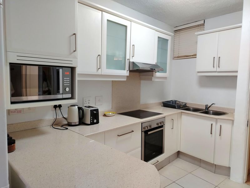 A functional kitchen featuring white cabinetry, stone-look countertops, a built-in oven, electric hob, extractor fan, and a double sink.