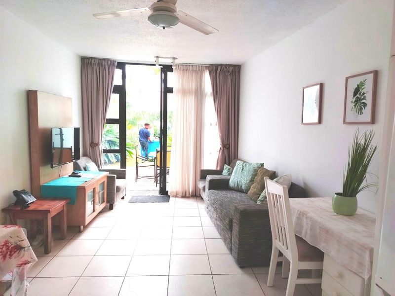 Open plan living area featuring tiled flooring, a ceiling fan, and large glass sliding doors providing direct access to the outdoor patio area.