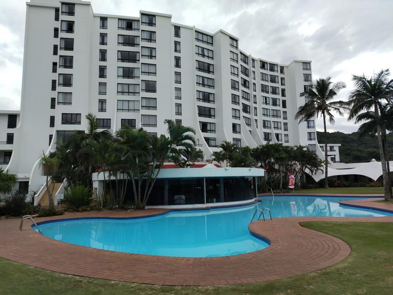 A view of the apartment complex exterior featuring a large swimming pool, landscaped garden areas, and multi-story building facade.