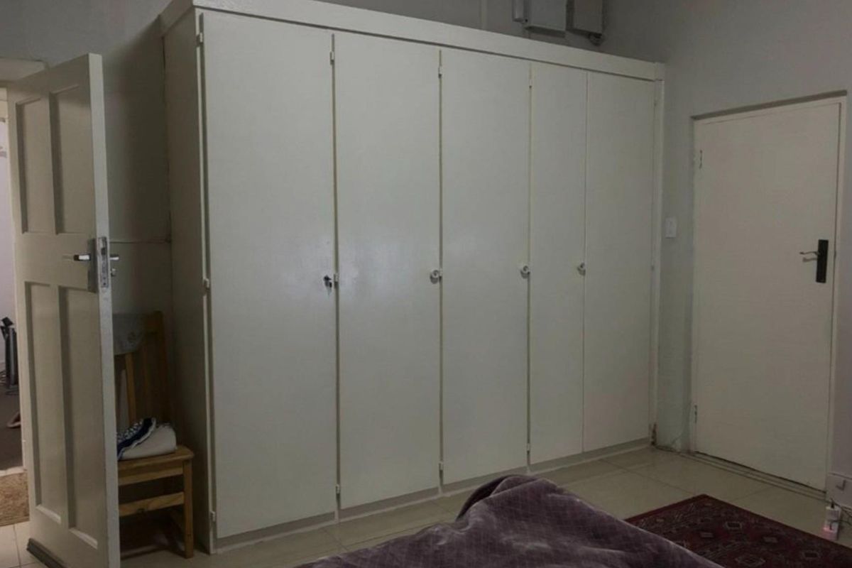A bedroom featuring extensive floor-to-ceiling built-in cupboards with white cabinetry and tiled flooring.
