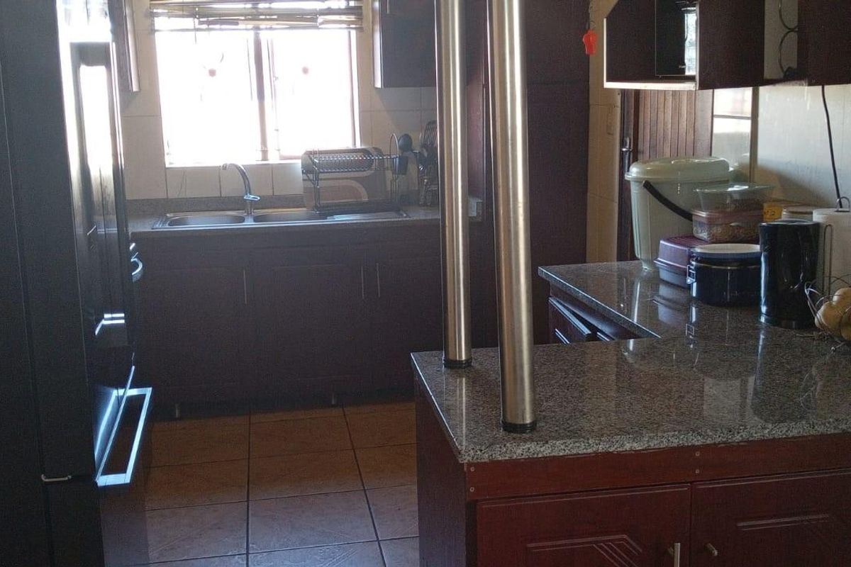 A functional kitchen featuring dark wood cabinetry, granite countertops, a double sink, and tiled flooring with a breakfast bar area.