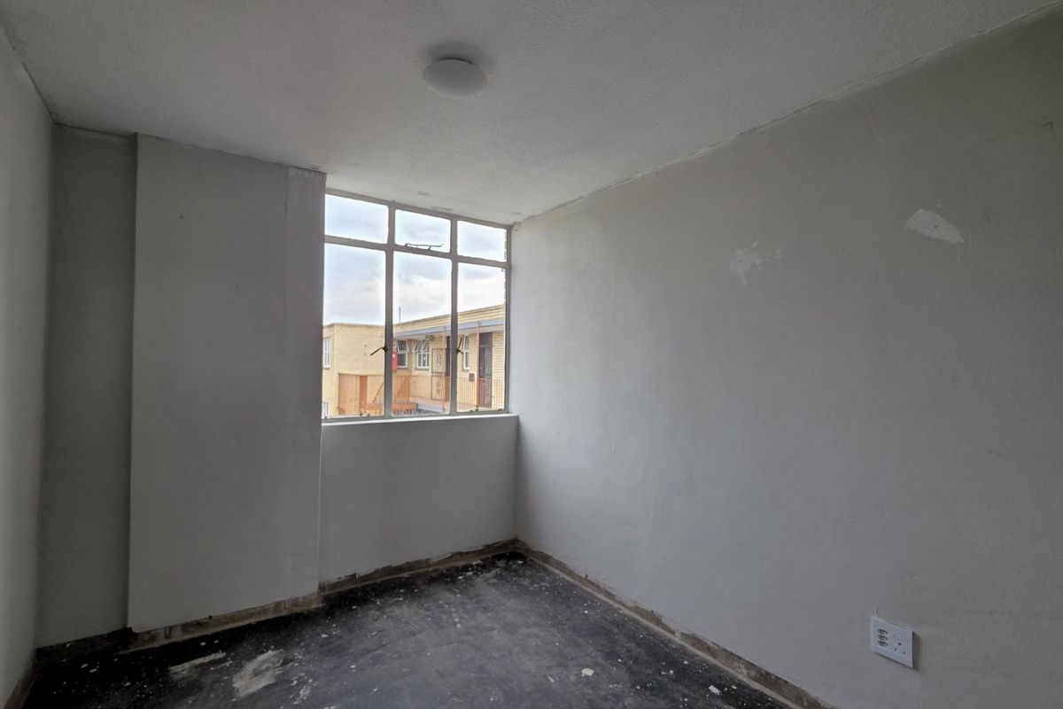 An empty bedroom featuring a large window, unfinished flooring, and plain walls, offering a blank canvas for renovation and interior design.