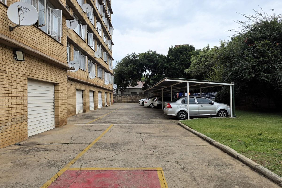 Exterior view of the apartment building featuring a paved driveway, multiple garage doors, and covered parking bays.