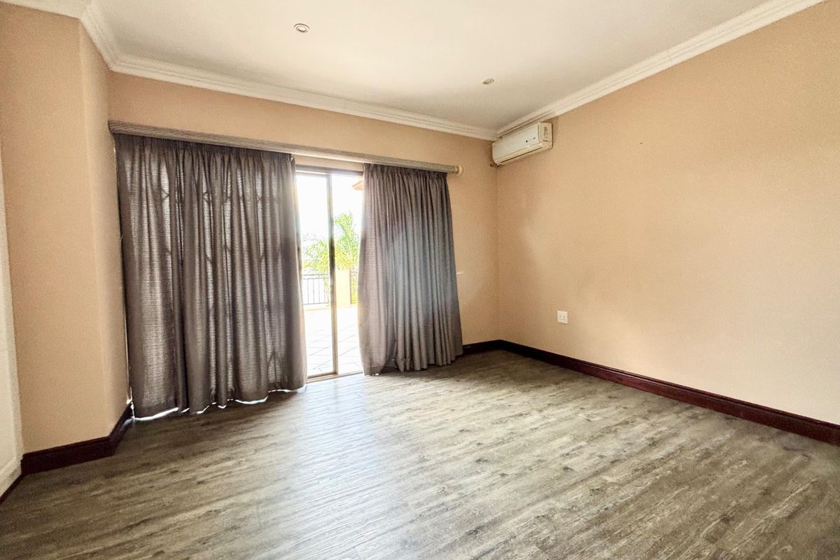 A spacious, empty bedroom featuring wood-look laminate flooring, crown molding, and a sliding glass door providing access to an outdoor area.