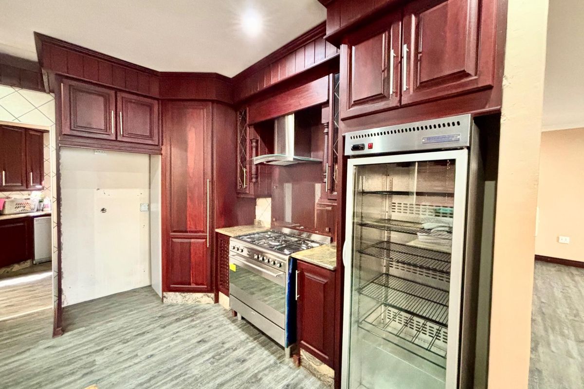 A kitchen featuring dark wood cabinetry, a stainless steel gas stove with extractor fan, and a glass-door display fridge.