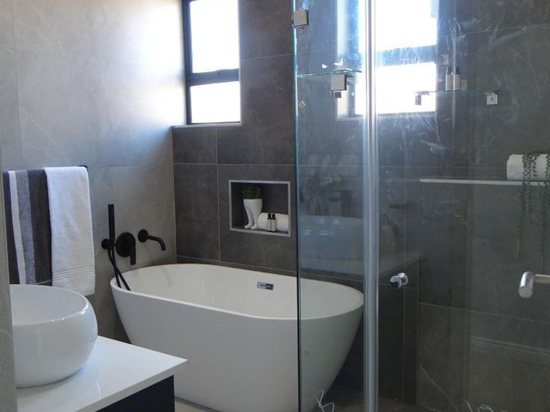 Modern bathroom featuring a freestanding bathtub, glass-enclosed shower, wall-mounted basin, and contemporary dark grey wall tiling.