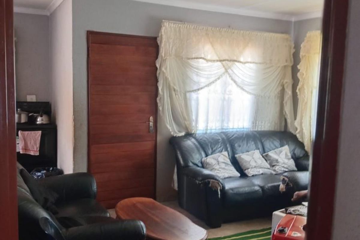 A living room area featuring tiled flooring, a solid timber door, and natural light through window treatments.
