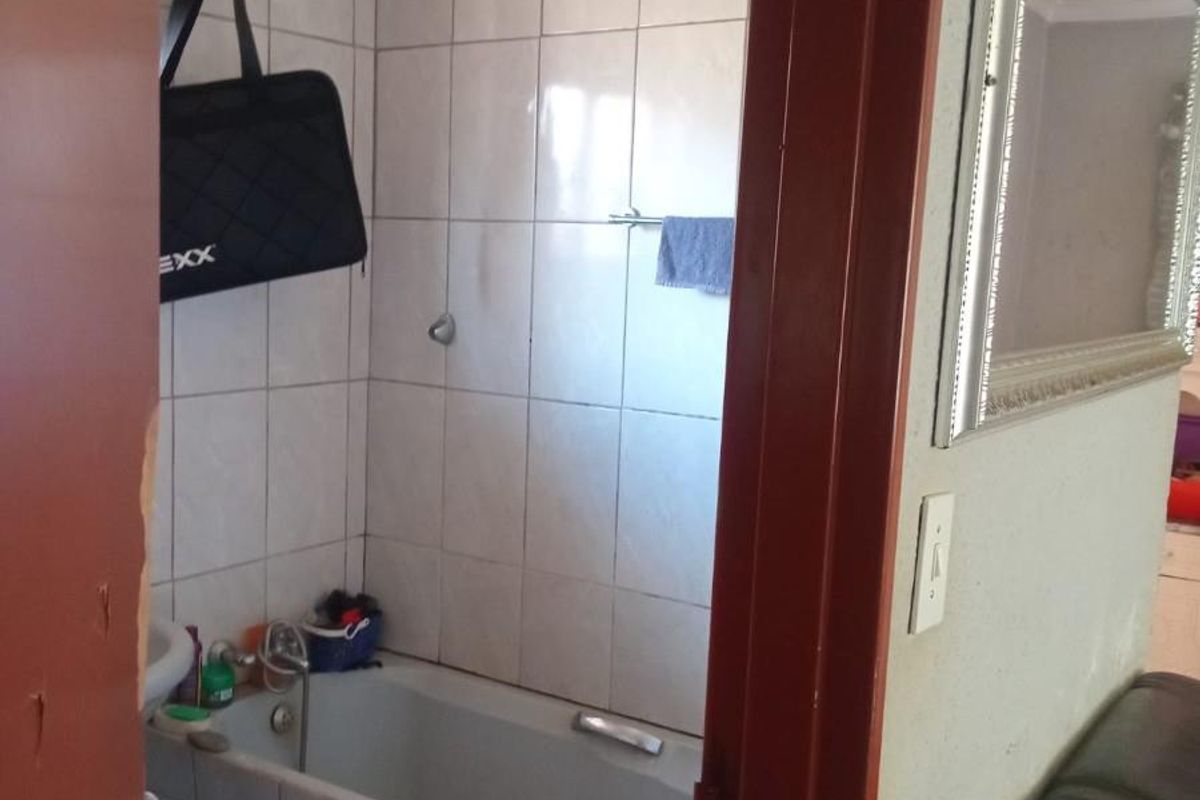 A compact bathroom featuring a tiled bathtub surround and wall tiling, viewed from the adjacent living area.